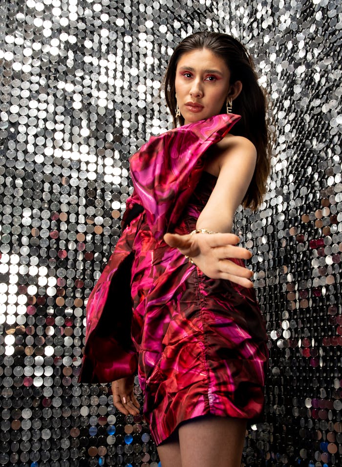 A striking portrait of a woman in a vibrant pink dress against a sequin background, exuding fashion and glamour.